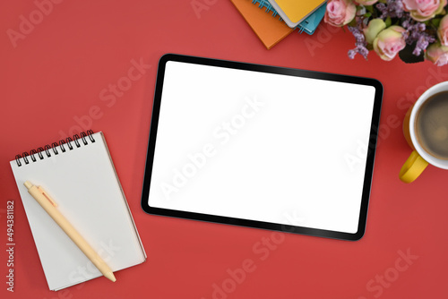 Top view mockup digital tablet with white screen, notepad and coffee cup on red background.