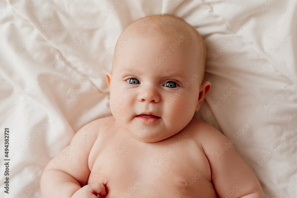 closeup portrait of a blue-eyed newborn baby lying on his back on a white sheet. happy carefree infancy. products for children, natural materials. space for text. High quality photo closeup portrait of a blue-eyed newborn baby lying on his back on a white sheet. happy carefree infancy. products for children, natural materials. space for text. High quality photo