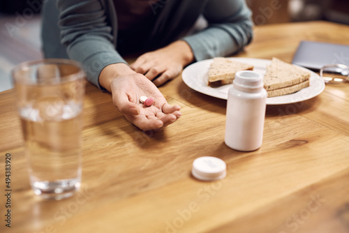 Close up of woman taking pills during breakfast at dining table.
