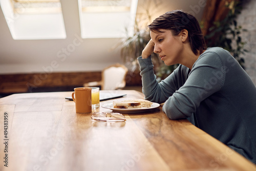 Thoughtful woman has no appetite while sitting at dining table at home.