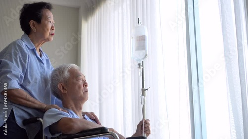 Wife comforting husband on wheel chair worry about health care older Asian elder senior couple in hosital photo