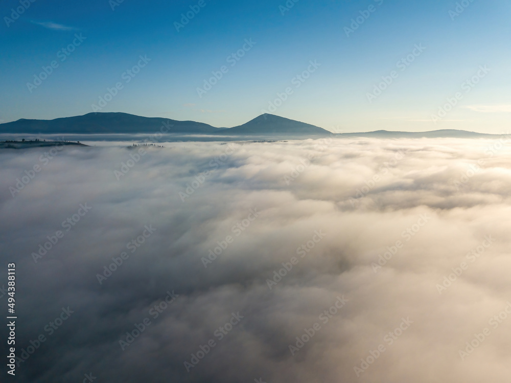 Flight over fog in Ukrainian Carpathians in summer. A thick layer of fog covers the mountains with a solid carpet. Mountains on the horizon. Aerial drone view.