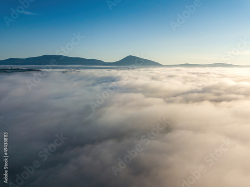 Flight over fog in Ukrainian Carpathians in summer. A thick layer of fog covers the mountains with a solid carpet. Mountains on the horizon. Aerial drone view.