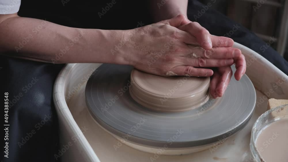 A woman works on a potter's wheel, making a mold out of clay with her hands in the workshop. A woman works on a potter's wheel, making a mold out of clay with her hands in the workshop.