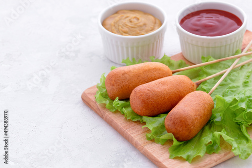 american fast food. corn dog with fresh lettuce, ketchup and mustard on a light background