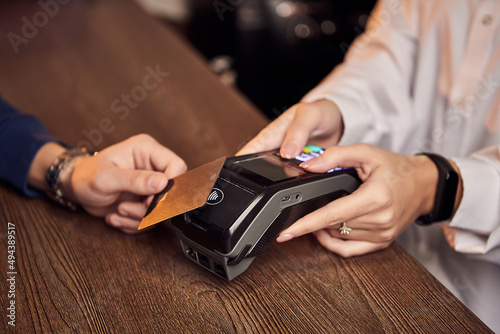 The customer's hand pays for a contactless credit card with NFC technology. Bartender with a Credit Card reader. Focus on hands. © bondvit