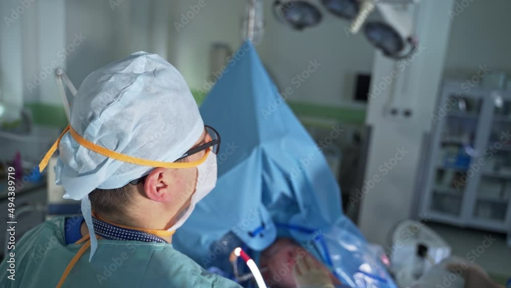 Adult surgeon moving the device tool input into patient. High angle view. Surgery room at backdrop in blur. Adult surgeon moving the device tool input into patient. High angle view. Surgery room at backdrop in blur.