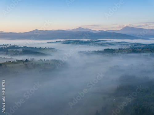 Flight over fog in Ukrainian Carpathians in summer. Mountains on the horizon. Aerial drone view.