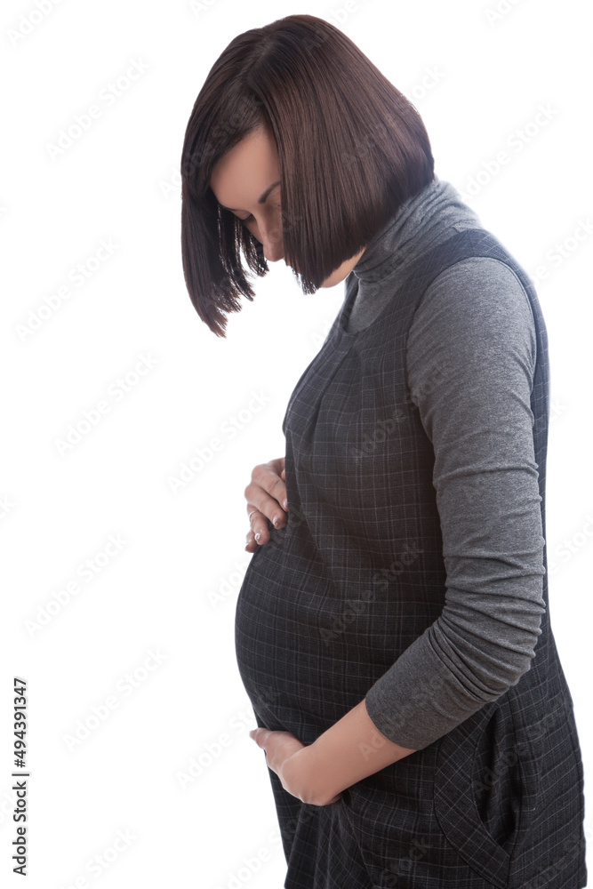 Portrait of Sensual Cute Positive Caucasian Brunette Pregnant Woman in Grey Dress Posing Over Pure White Background While Looking Down. Portrait of Sensual Cute Positive Caucasian Brunette Pregnant Woman in Grey Dress Posing Over Pure White Background While Looking Down.