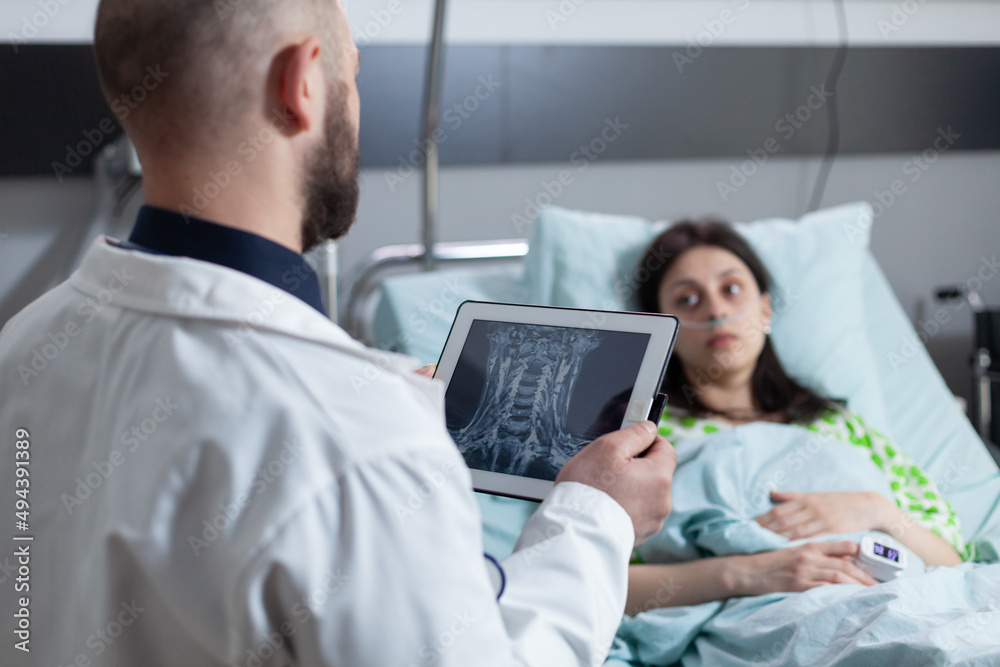 Doctor holding digital tablet with mri scan of throat area reading diagnosis to concerned patient on hospital bed recieving oxygen. Medic explaining cervical injury to woman with low spo2 saturation.