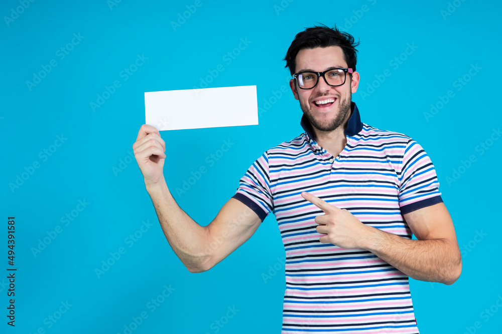 Happy Caucasian Handsome Man Posing in Striped Shirt and Hipster Glasses Smiling Looking Straight to Camera While Holding Empty White Paper Sheet Over Blue. Happy Caucasian Handsome Man Posing in Striped Shirt and Hipster Glasses Smiling Looking Straight to Camera While Holding Empty White Paper Sheet Over Blue.