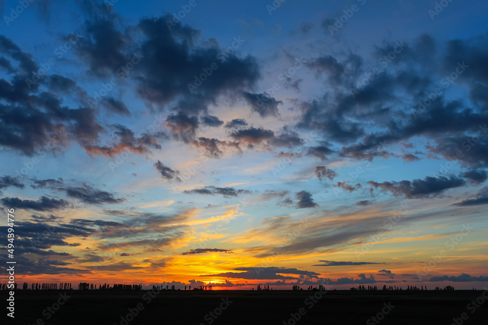 A bright, colorful sunset in the countryside. An orange-blue sky with clouds hangs over a field. A beautiful sundown. A bright, colorful sunset in the countryside. An orange-blue sky with clouds hangs over a field. A beautiful sundown.