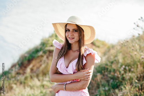 a young brunette woman stands in the middle of a field in a white dress and a straw hat. girl posing in a lavender field. a woman enjoys the sun with her eyes closed.