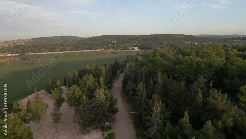 Aerial drone shot over a green forest in Latrun in Israel at sunset over a hilly terrain with the view of a busy highway in the background. photo