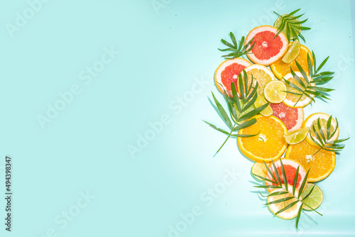 Colorful flatlay of citrus fruit slices and tropical palm leaves. Orange, grapefruit, lemon, lime bright high-colored slices on turquoise blue background. Summer holiday background top view