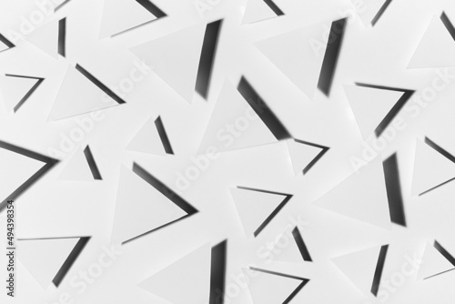 White paper triangles different size as abstract random pattern in bright light with black strict shadows, top view. Contemporary simple abstract background.