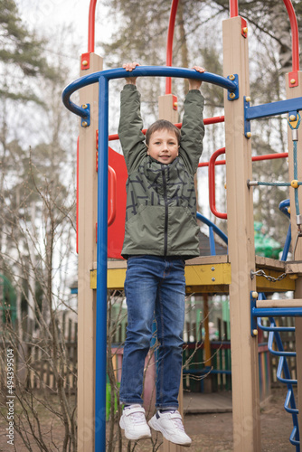 Happy teenager boy playing on kids playground. Outdoor activity. Portrait of joyful child in green jacket having fun outdoors. Carefree childhood.