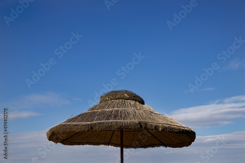Straw beach umbrella against the backdrop of a sunny sky.