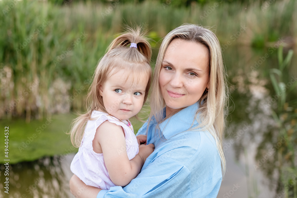Caucasian Mother with a toddler daughter hugging enjoying outdoors by the river or lake in summer. Happy family portrait. Spending family time together. Single parent