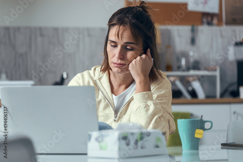 Fotografia Illness young woman feeling bad while working with laptop sitting in the kitchen at home