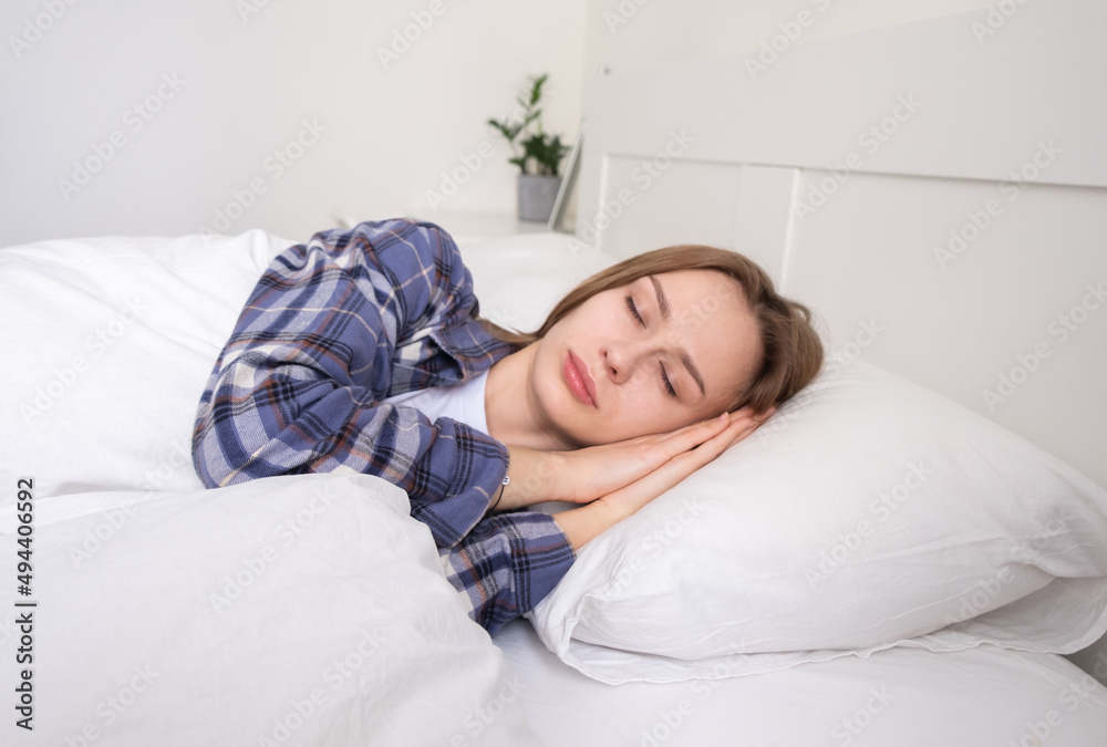 A girl sleeps in pajamas on a white bed. A young woman lies with her eyes closed under the blanket. A cozy woman's morning. A girl sleeps in pajamas on a white bed. A young woman lies with her eyes closed under the blanket. A cozy woman's morning.