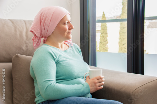 Fotografie Young woman with cancer in head scarf relaxing drinking coffee sitting on a sofa