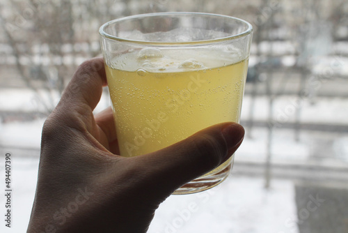 The glass is full of water with a round tablet dissolving with bulbs. A glass in a female hand near a window overlooking the winterstreet, close-up, top view. Poppy tablet. Vitamins. photo