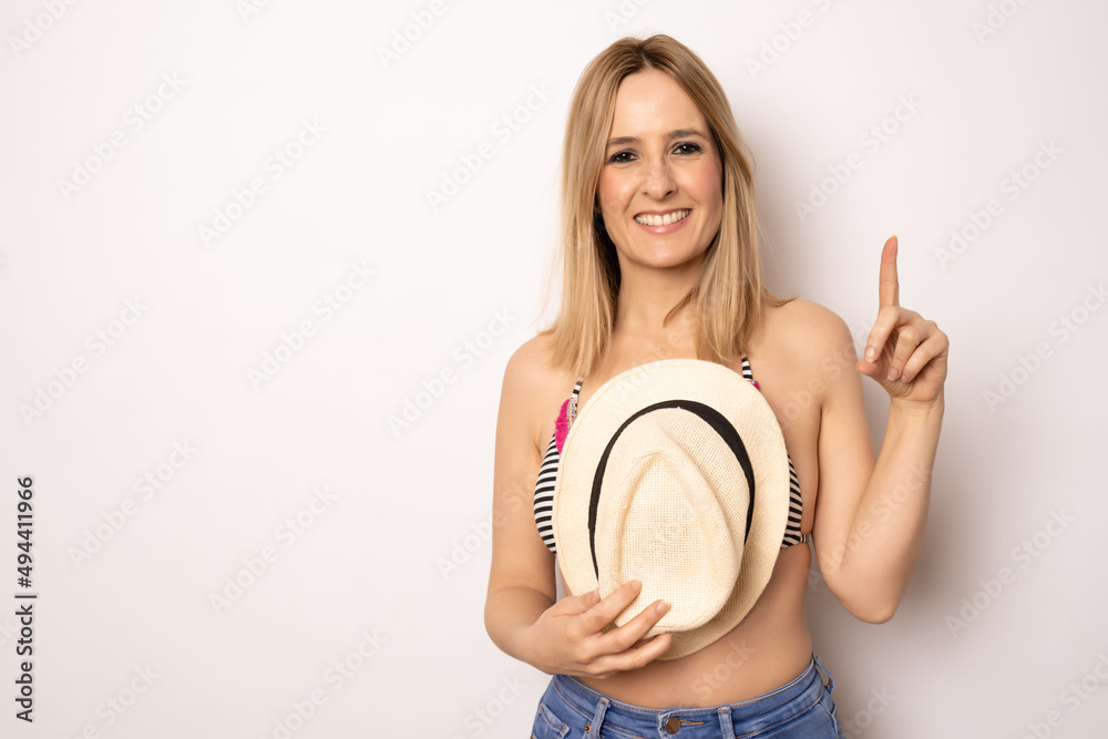 Happy woman in summer outfit pointing finger up standing isolated over white background.