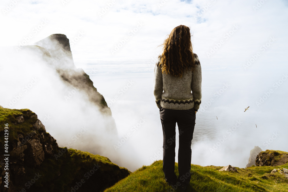 Naklejka premium woman on a cliff in front of the ocean on a foggy day