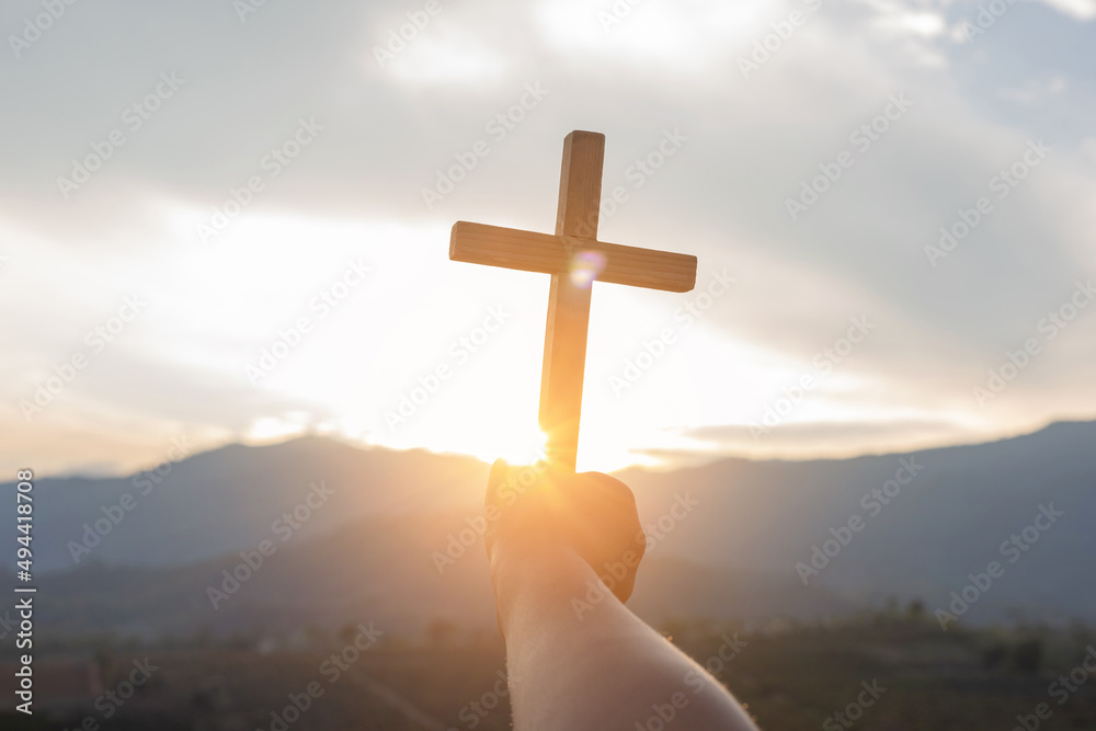 Human hand praying and holding a Christian cross for worship.