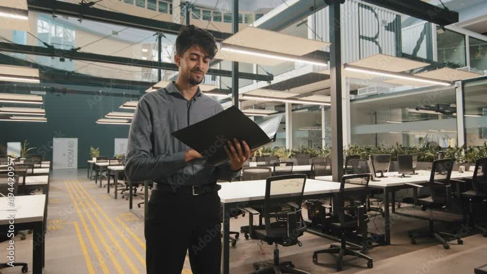 Young indian latin manager male business man employee checking document folder inspecting financial report raising head with satisfied look winking eye approvingly giving consent working agreement Young indian latin manager male business man employee checking document folder inspecting financial report raising head with satisfied look winking eye approvingly giving consent working agreement