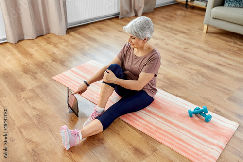 sport, fitness and healthy lifestyle concept - smiling senior woman exercising with tablet pc computer on mat at home