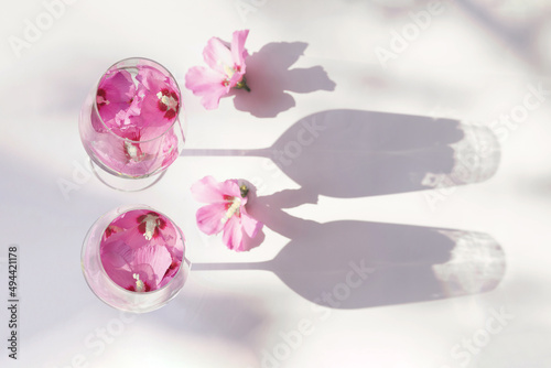 Creative composition made of two glasses with hibiscus flower water on white background with sunlit. Summer and refreshment concept. Minimal style