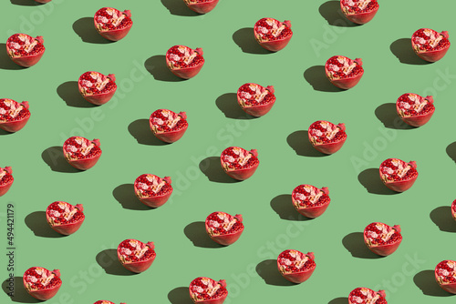 Creative pattern made of half fresh pomegranates on green background with shadows. Refreshment concept. Healthy food ingredient theme.