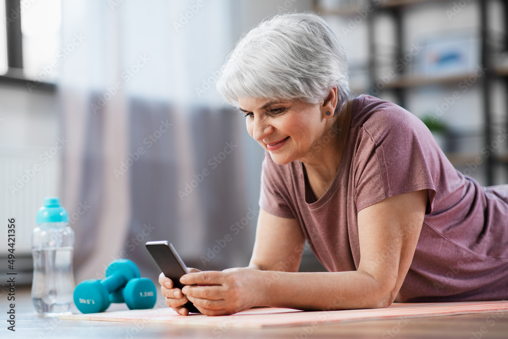 sport, fitness and healthy lifestyle concept - smiling senior woman with smartphone exercising on mat at home