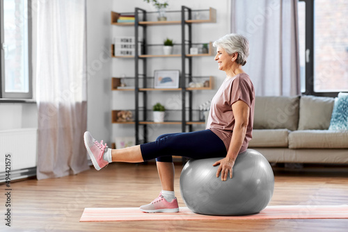 sport, fitness and healthy lifestyle concept - smiling senior woman training by sitting on exercise ball at home photo