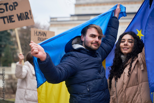 Man and woman covered with EU and Ukraine flags and showing peace sign