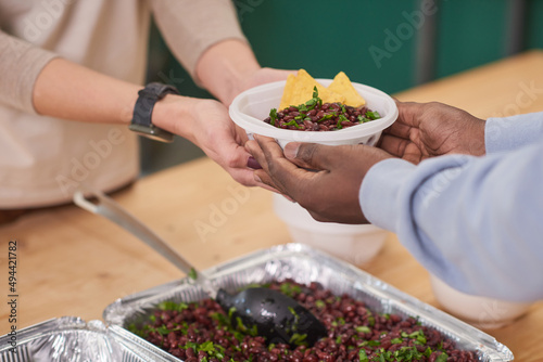 Medium close-up shot of unrecognizable volunteer giving plate with meal to beneficiaries in charity canteen