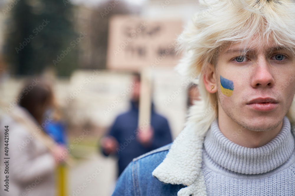 Close up of young caucasian man with Ukrainian flag painted on his cheek
