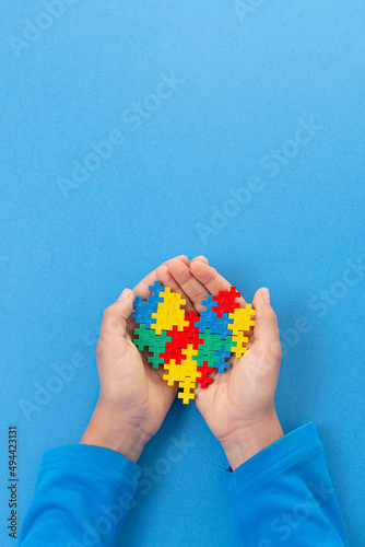 World autism awareness day concept. Child hand holding colorful puzzle heart on light blue background