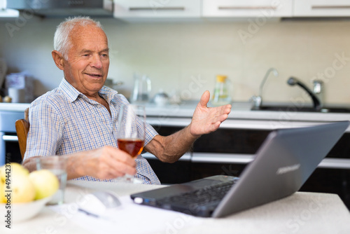 Senior man with glass of brandy and laptop