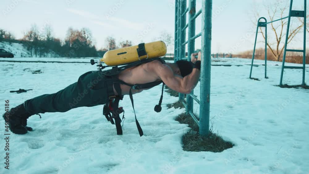 Bodybuilder With A Naked Torso Doing Push Ups From The Bar In The Cold With A Drager On His Back