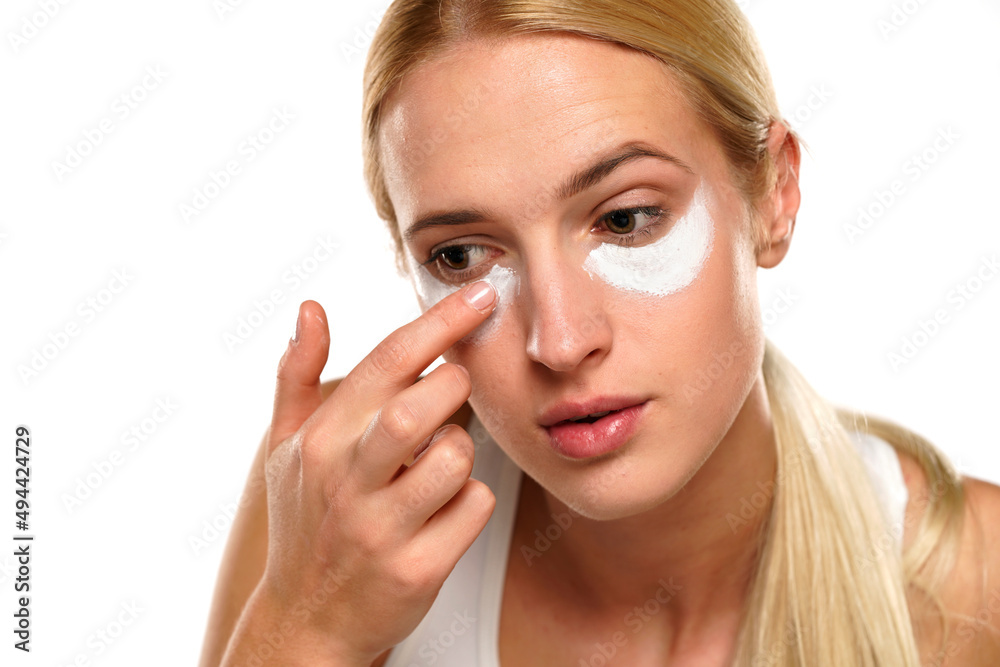 portrait of a young blond woman applying cosmetic product under her eyes portrait of a young blond woman applying cosmetic product under her eyes