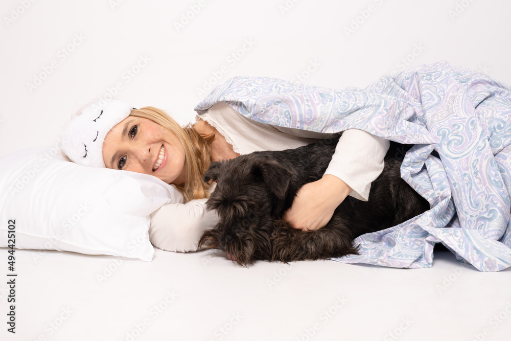 Smiling young woman in pajamas laying on pillow with her dog isolated on white background. Smiling young woman in pajamas laying on pillow with her dog isolated on white background.