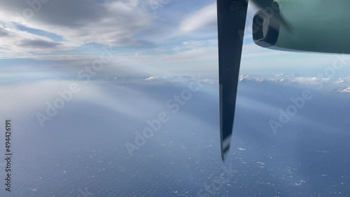 Domestic Aircraft Norway, turboprop engine, Filmed out of window above arctic northern Norway, with snow capped mountings, beams of light, and clouds, Lofoten Island in the background,tilt upward shot photo