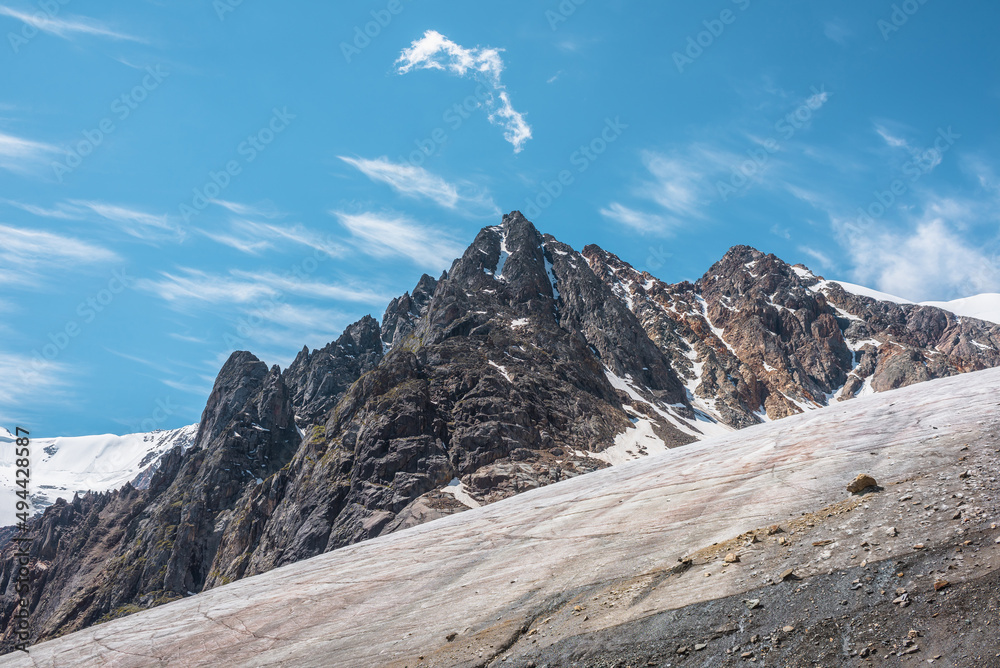 Scenic mountain landscape with glacier under sharp rocks in sunlight. Awesome landscape with glacial tongue and rocky pinnacle in sunshine. Beautiful view to snow mountains at very high altitude.