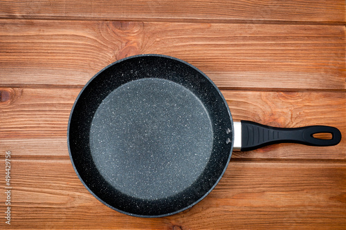 A round frying pan with a plastic handle is a utensil for frying food. Taken against the backdrop of a wooden table surface.