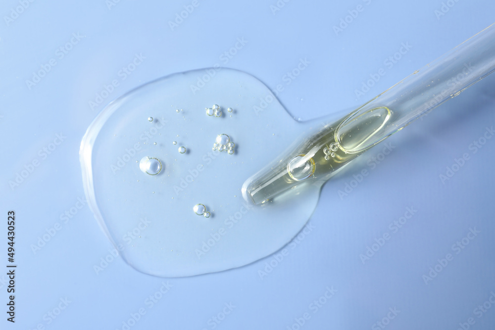 Dripping hydrophilic oil from pipette on light blue background, top view Dripping hydrophilic oil from pipette on light blue background, top view