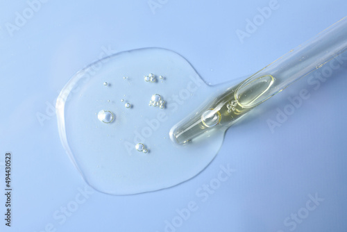 Dripping hydrophilic oil from pipette on light blue background, top view
