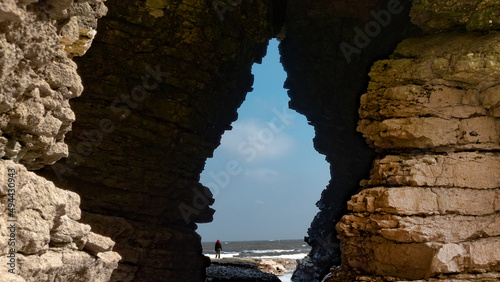 Woman standing in front of ocean as seen through rock formation arch